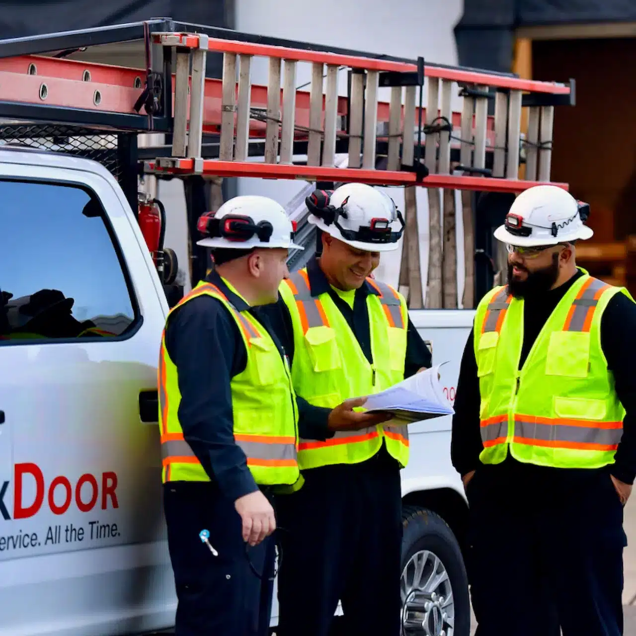 Three people in high-visibility vests in front of an Allmark Door truck